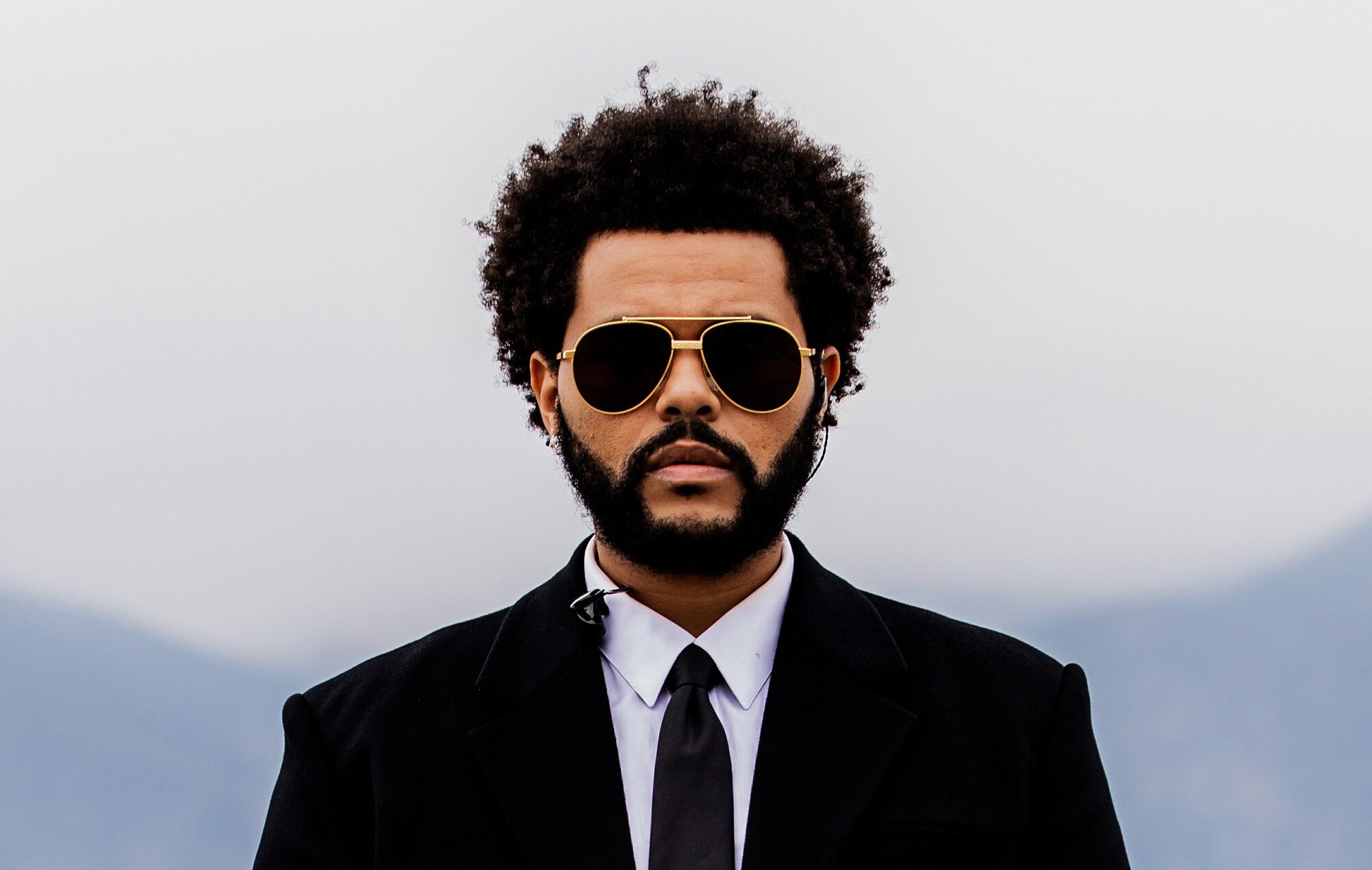 The Weeknd — retrato oficial con gafas doradas y traje negro